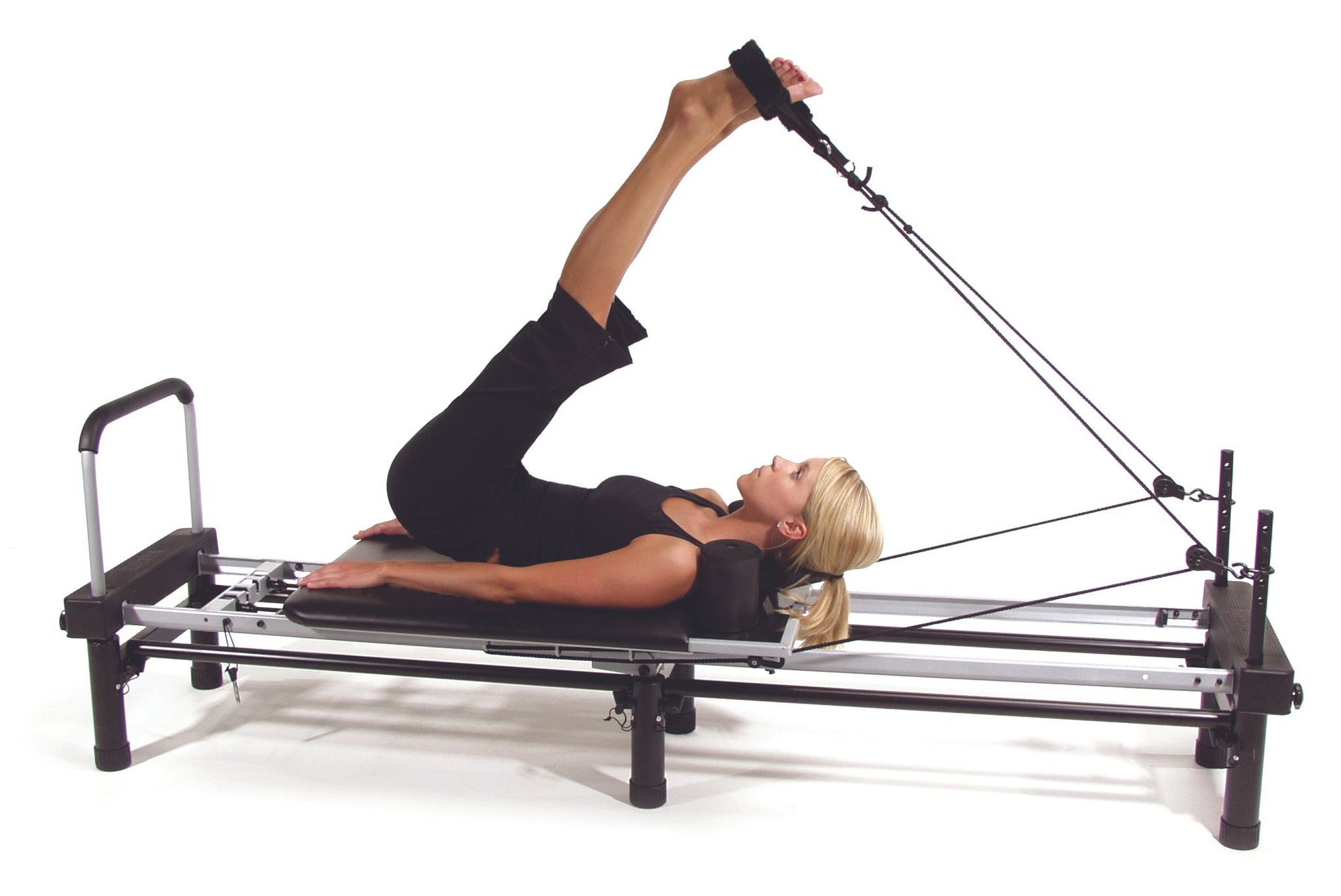 Woman demonstrating  reformer pilates machine with legs in straps and on stand